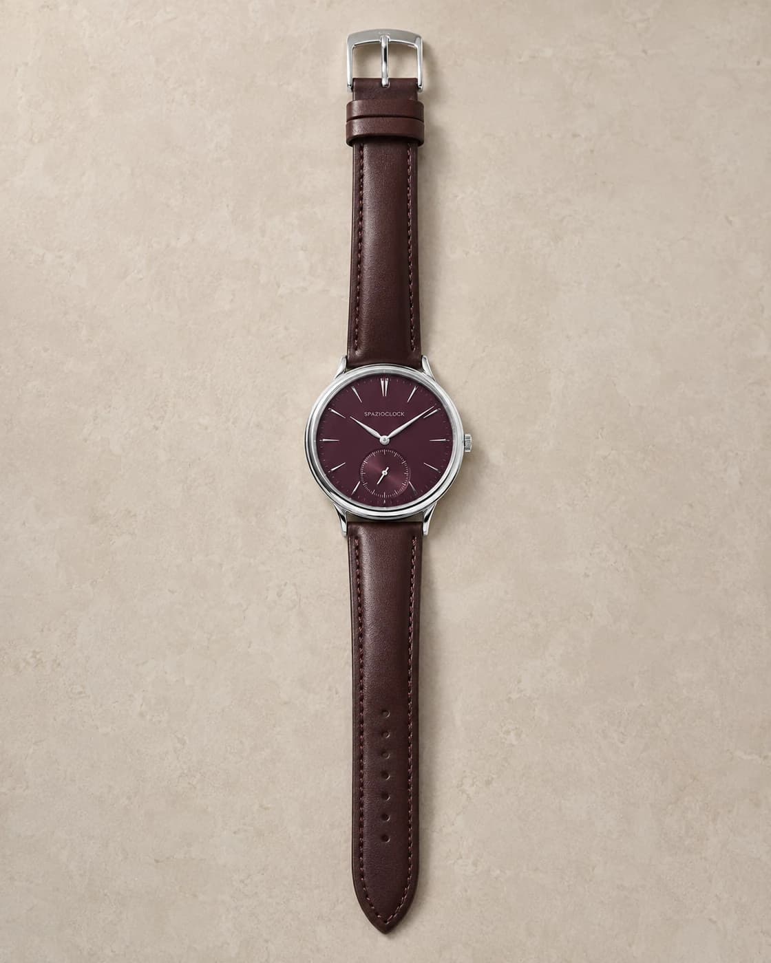 Meridiano II de Spazioclock, reloj en burdeos fotografiado sobre fondo piedra